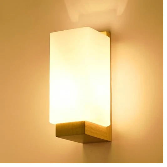 Modern indoor wall light with frosted rectangular shade and wooden base, emitting a warm ambient glow.