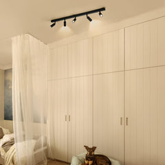 Dog sitting on a bed in a bedroom with a large wardrobe and track lights.