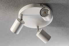 Ceiling light fixture with three white cylindrical lamps on a gray ceiling.