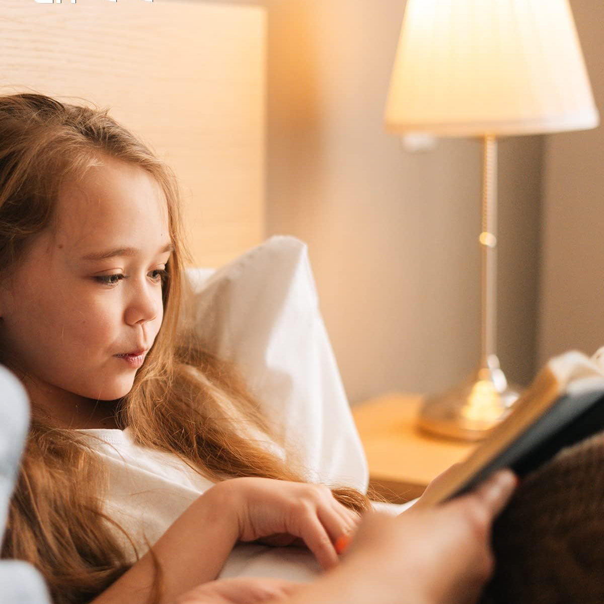 Child reading a book in bed with a lamp on a nightstand, featuring UKCA and CE logos.