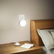 Wall-mounted night light above a wooden bedside table with a book and cup.