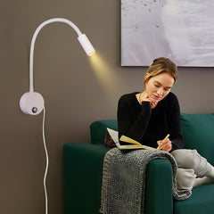 Woman reading on a green couch with a wall-mounted lamp illuminating her.