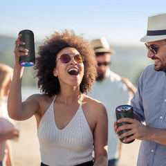 Two people holding portable speakers outdoors with a clear sky background