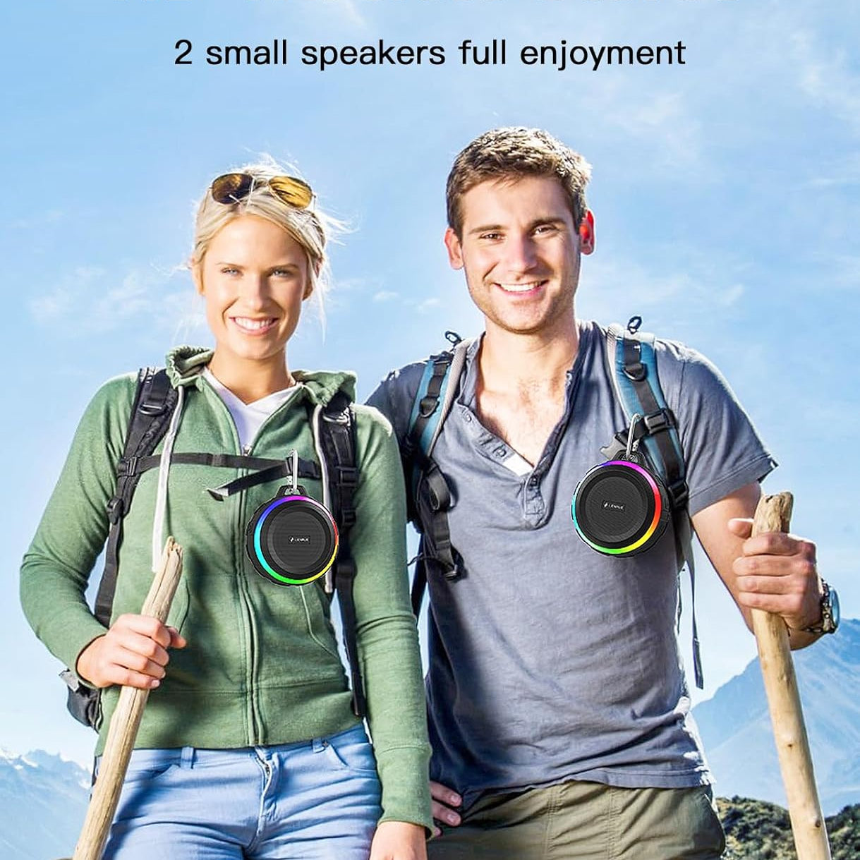 Two people hiking with wireless stereo speakers on backpacks against a mountainous background.