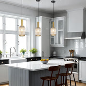 Modern kitchen with white island, wooden chairs, and pendant lights.