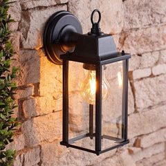 Black outdoor wall lantern with a lit bulb attached to a stone wall.