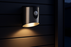Black outdoor wall light fixture with motion sensor on a dark wooden surface