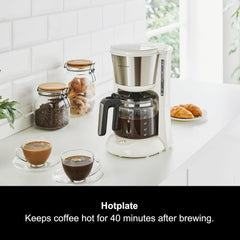 Coffee maker on a kitchen counter with two cups of coffee and jars of coffee beans.
