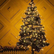 Decorated Christmas tree with lights against a yellow wall.