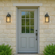 Gray front door with glass panels on a stone wall with outdoor lights.