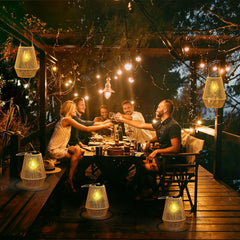 Group of people enjoying a meal outdoors with string lights and lanterns.