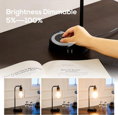 Hand adjusting a dimmable lamp on a table with a book open below.