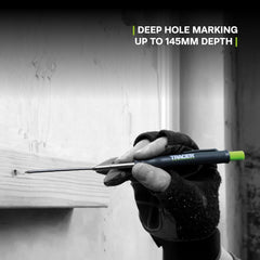 Hand holding a tool with 'Tracer' branding marking a deep hole on a wooden surface.