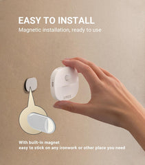 Hand holding a white device with text about magnetic installation on a beige background