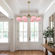 Modern chandelier with pink glass shades in a bright room with wooden floor and white walls.