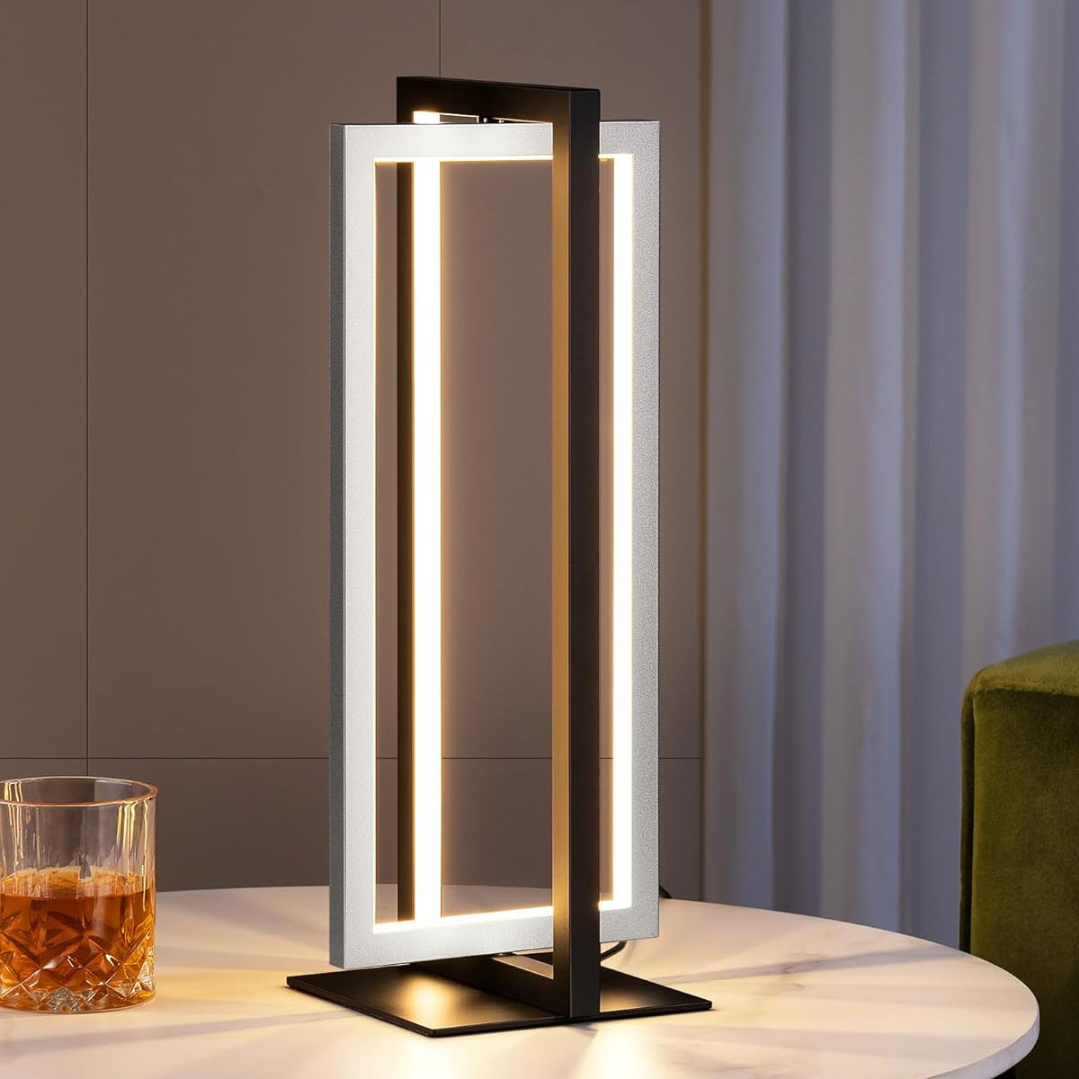 Modern table lamp on a round table with a glass of whiskey in a dimly lit room.