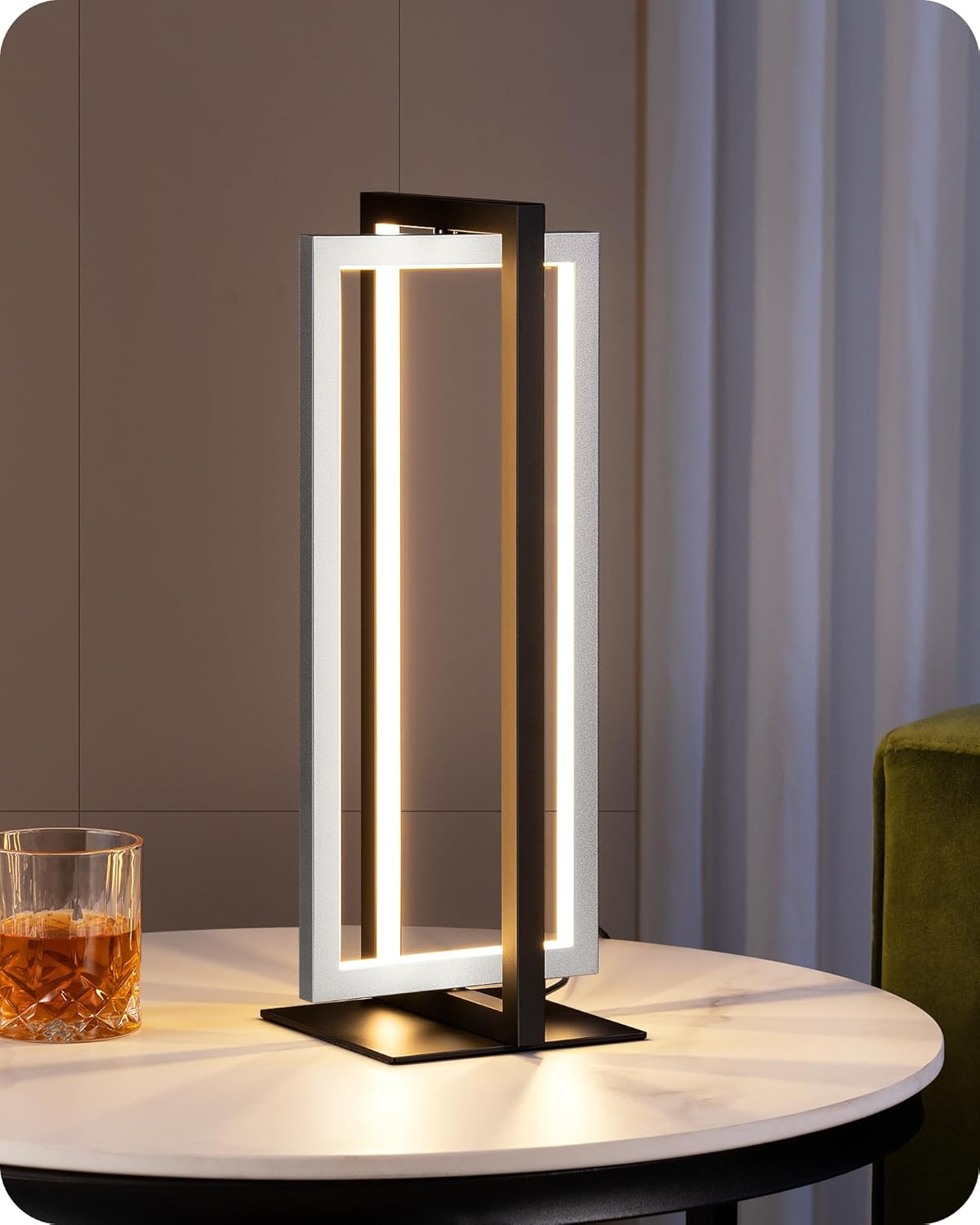 Modern table lamp on a round table with a glass of whiskey in a dimly lit room.