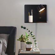 Modern wall-mounted lamp with a candle and decorative plants on a table.