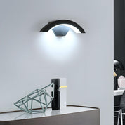 Modern wall-mounted light fixture on a white wall with a desk and chair in the foreground.