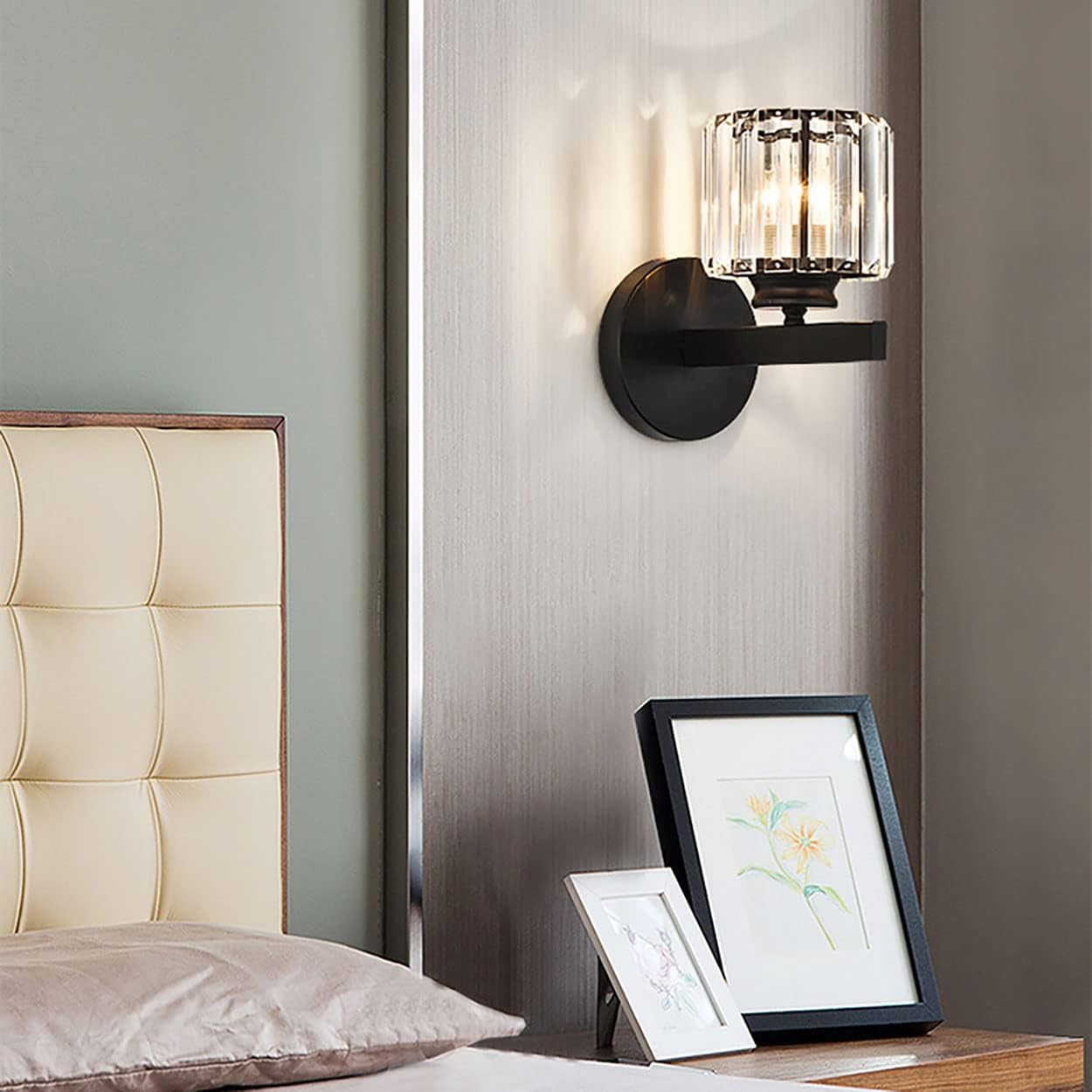 Modern wall sconce on a neutral wall with a bed and framed pictures in the foreground.