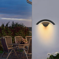 Outdoor wall light fixture on a white wall with a patio table and chairs in the background.