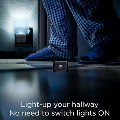 Person wearing checkered pajama pants and slippers standing next to a night light on a dark floor.