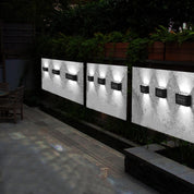 Three outdoor wall lights on a concrete wall with a garden and pathway in the background.