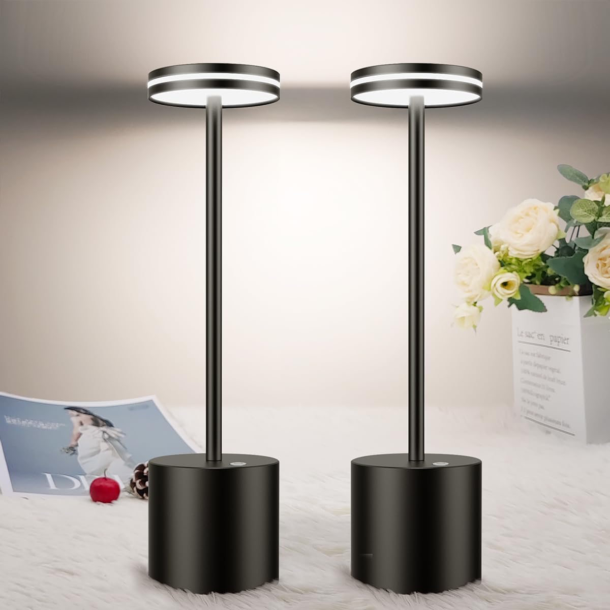 Two black floor lamps on a light-colored surface with flowers and a magazine in the background.