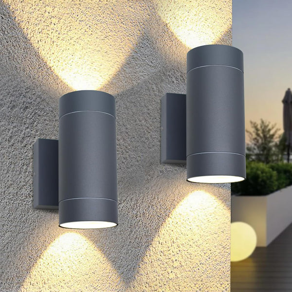 Two cylindrical outdoor wall lights on a textured stone wall with a blurred garden background.