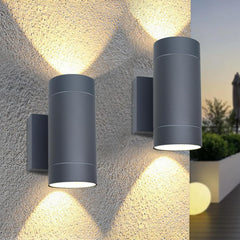 Two cylindrical outdoor wall lights on a textured stone wall with a blurred garden background.