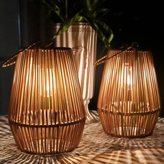 Two woven rattan lanterns with a vase in the background on a textured surface.
