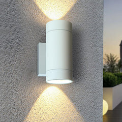 White outdoor wall light fixture on a textured gray wall with a scenic background.