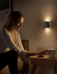 Woman sitting in a dimly lit room with a small table and light fixture.