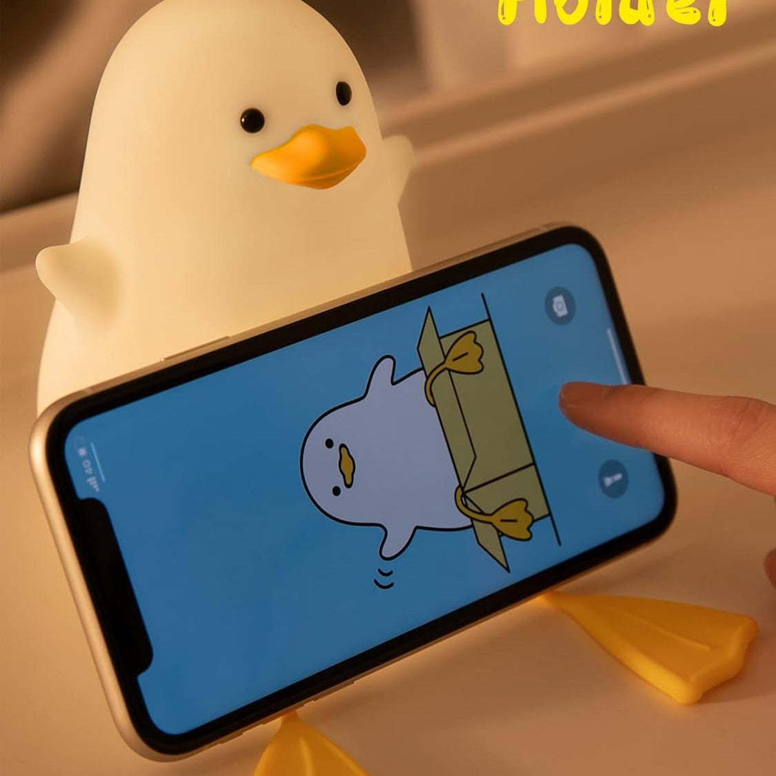 Yellow duck-shaped phone holder with a smartphone displaying an animated character on a beige surface.